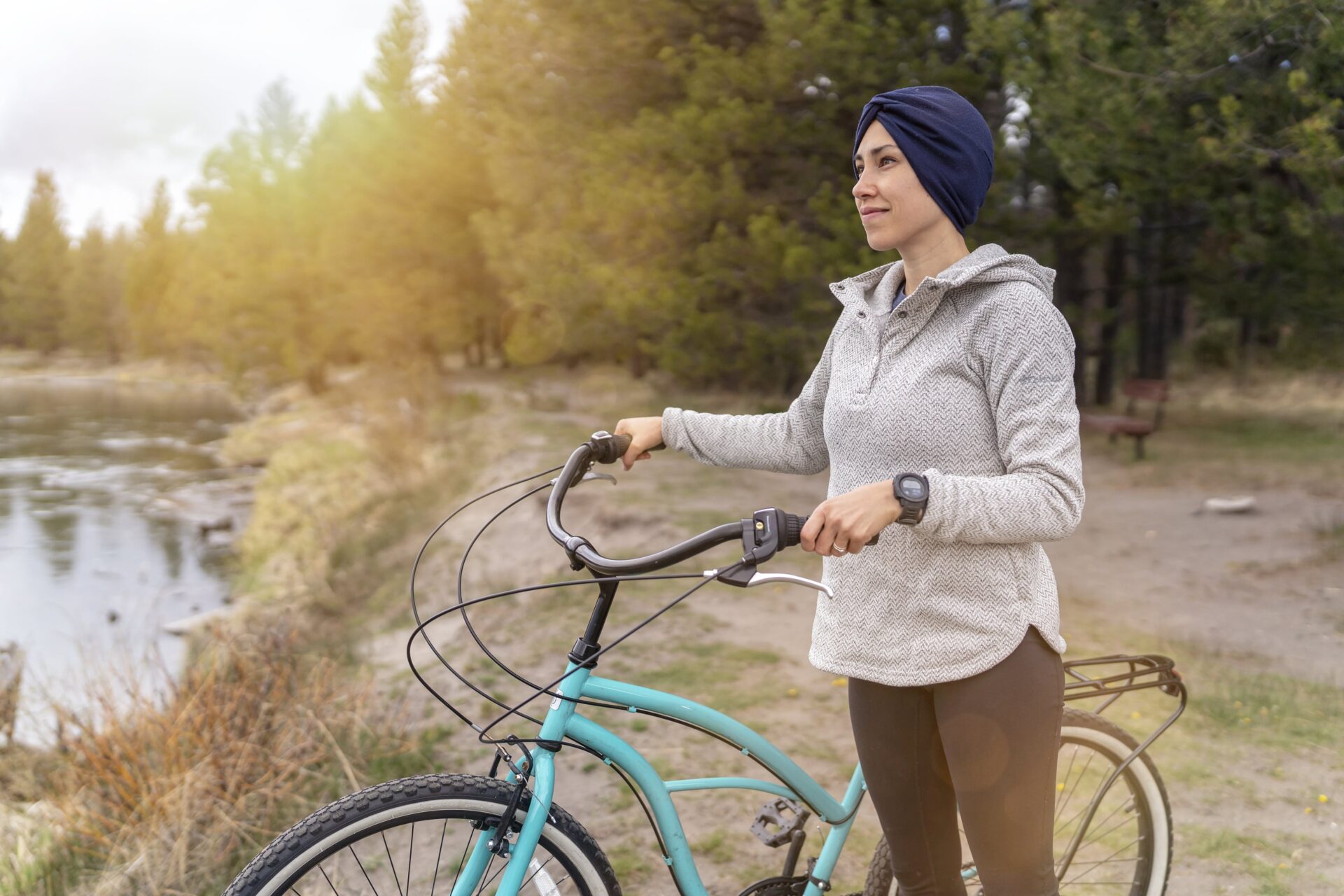 A young woman standing in the forest holding her blue bike.