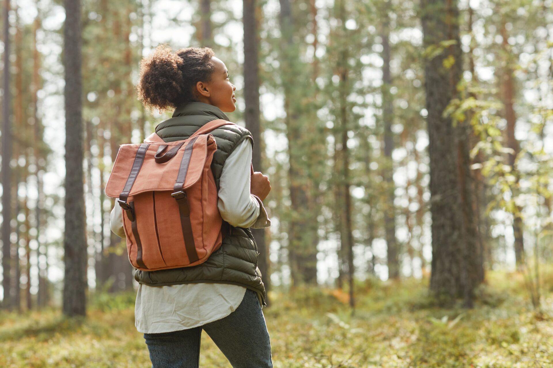 A young woman with an orange backpack hiking in the forest.