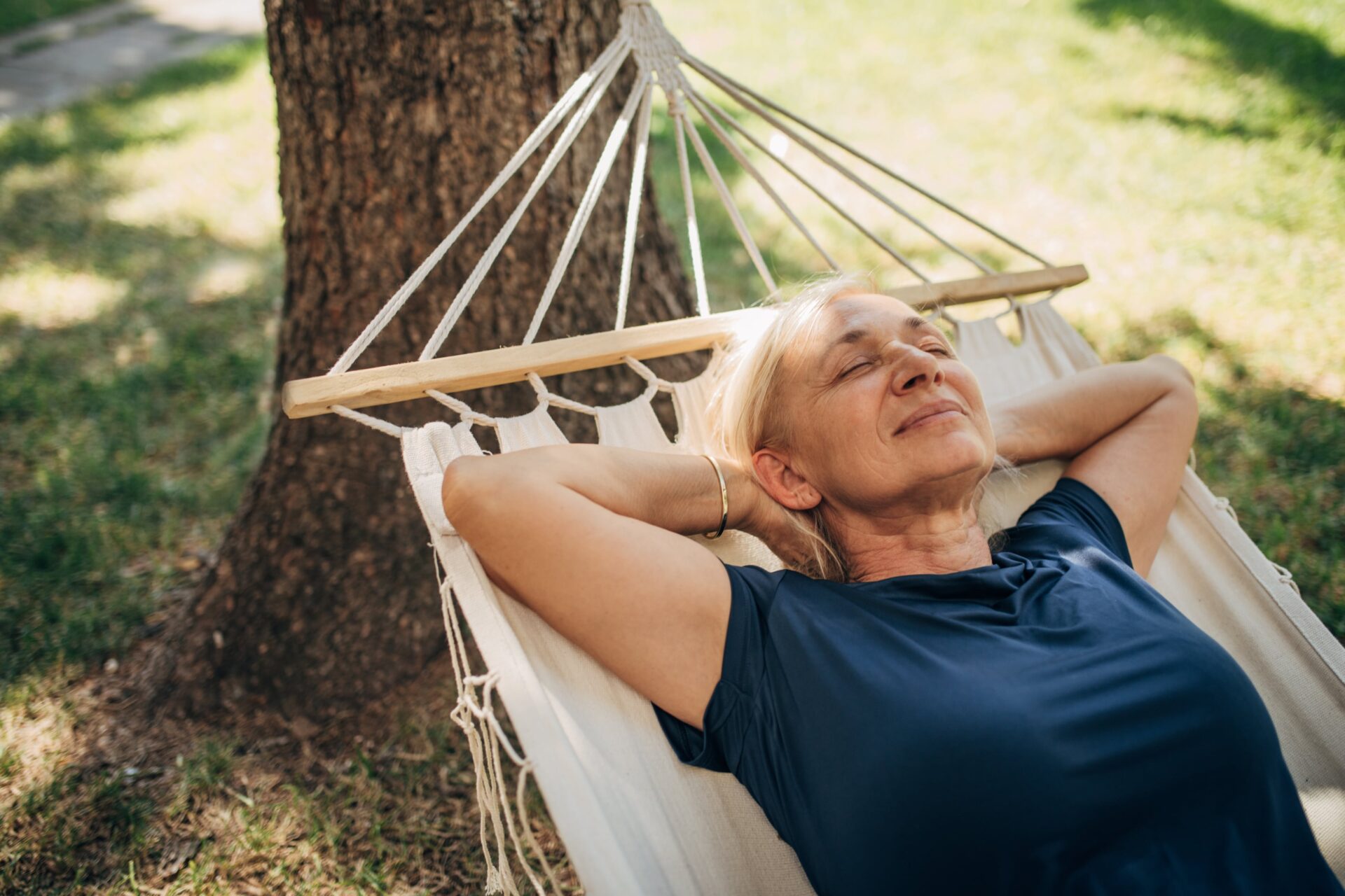 An older woman relaxing on a hammock outside in the sun with her eyes closed.