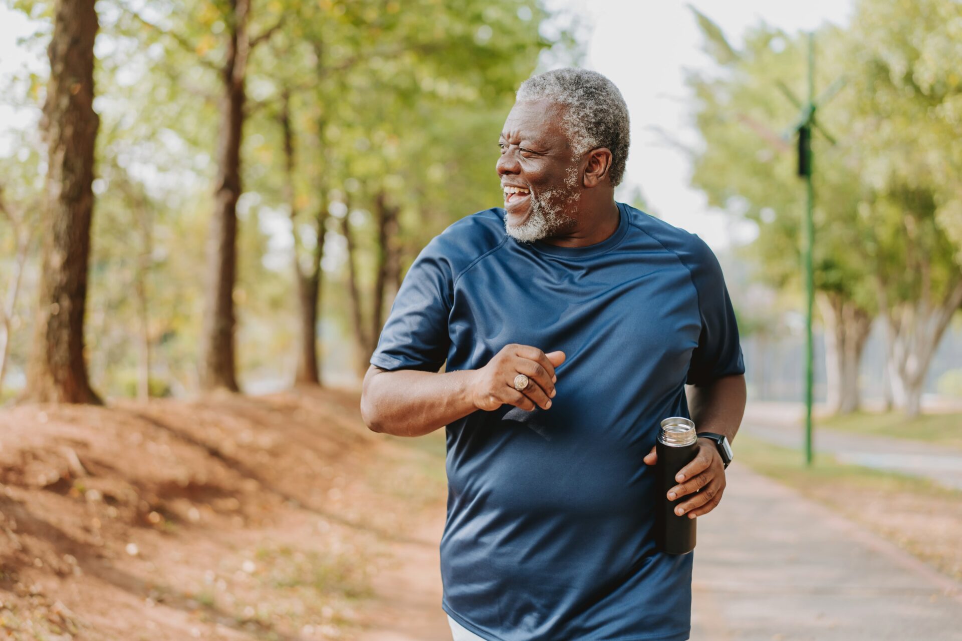 An older man smiling and going for a jog with water outside on a sunny day.