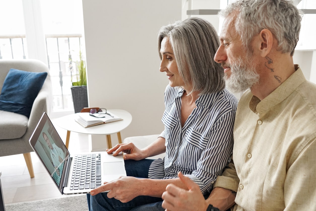 Image: A man and a woman sit together on a couch, engaging in a virtual support group session displayed on a laptop screen. They are attentively participating, highlighting the supportive nature of online communities.